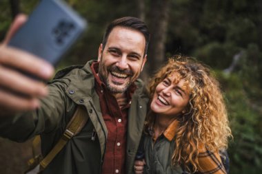 Karı koca yürüyüşçüleri sırt çantasıyla gezerler. Ormanda yürüyüş yaparken kendi portresini ya da video görüntülerini çekerler.