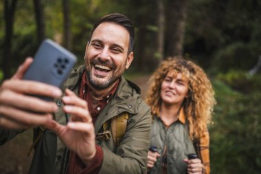 Yetişkin adam yürüyüşçüsü karısı arkasında dururken kendi fotoğrafını çeker.