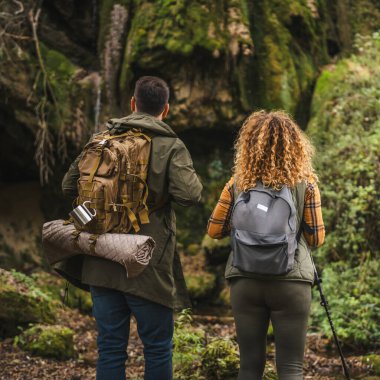 Yürüyüş yapan çiftin arka manzarası. Karı koca, şelalenin önünde yürüyüş çubuklarıyla.