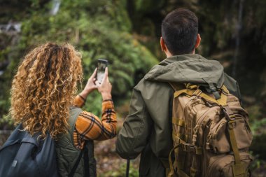 Yürüyüşçü çiftin arka görüntüsü. Karı koca şelalenin fotoğrafını çekiyor.