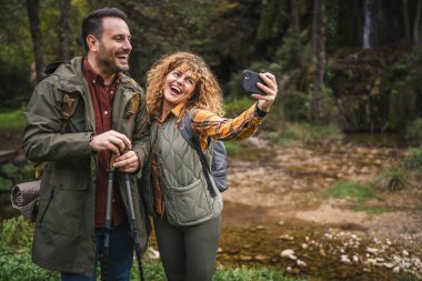 Karı koca yürüyüşçüleri sırt çantasıyla gezerler. Ormanda yürüyüş yaparken kendi portresini ya da video görüntülerini çekerler.