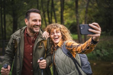 Karı koca yürüyüşçüleri sırt çantasıyla gezerler. Ormanda yürüyüş yaparken kendi portresini ya da video görüntülerini çekerler.