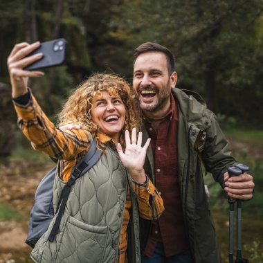 Karı koca yürüyüşçüleri sırt çantasıyla gezerler. Ormanda yürüyüş yaparken kendi portresini ya da video görüntülerini çekerler.