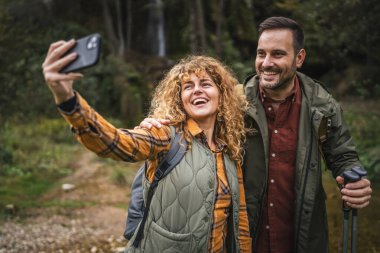 Karı koca yürüyüşçüleri sırt çantasıyla gezerler. Ormanda yürüyüş yaparken kendi portresini ya da video görüntülerini çekerler.