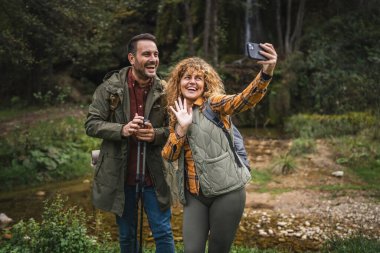 Karı koca yürüyüşçüleri sırt çantasıyla gezerler. Ormanda yürüyüş yaparken kendi portresini ya da video görüntülerini çekerler.