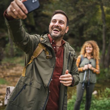 Yetişkin adam yürüyüşçüsü karısı arkasında dururken kendi fotoğrafını çeker.