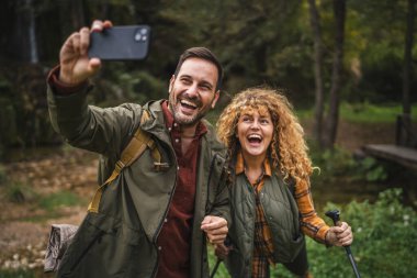 Karı koca yürüyüşçüleri sırt çantasıyla gezerler. Ormanda yürüyüş yaparken kendi portresini ya da video görüntülerini çekerler.