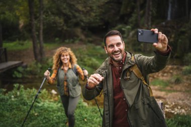 Yetişkin adam yürüyüşçüsü karısı arkasında dururken kendi fotoğrafını çeker.