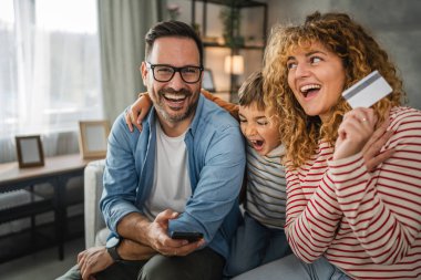 Anne, baba ve oğul evde kredi kartıyla internet üzerinden alışveriş yapıyorlar.