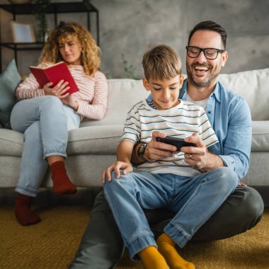 Baba ve oğul ve anne arkada cep telefonuyla oyun oynuyorlar.