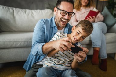 Baba ve oğul ve anne arkada cep telefonuyla oyun oynuyorlar.