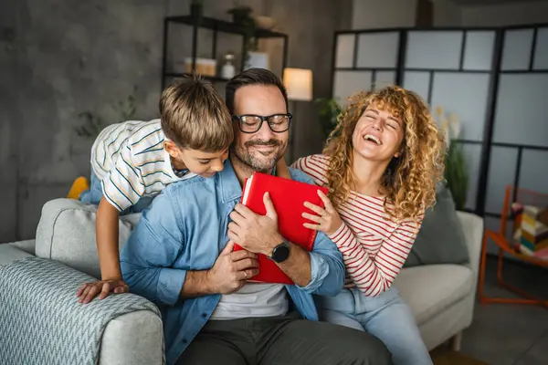 Baba aile albümüne sarıldı ve oğluyla karısına kanepede oturdu.