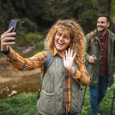 Yetişkin bir kadın yürüyüşçü kocası arkada dururken kendi portresini ya da görüntüsünü çeker.