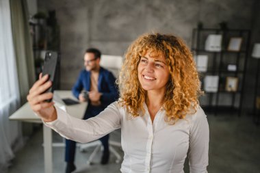 İş kadınının portresi cep telefonuyla ofisteki cep telefonundan görüntülü arama yapıyor.