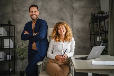 Yetişkin bir iş kadınının portresi ofiste erkek meslektaşının arkasında oturuyor.