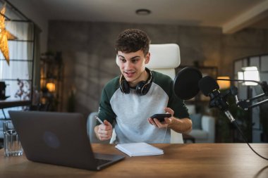 Young man blogger prepare for new video at home studio and take photo of notes with mobile phone clipart