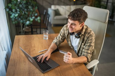 Genç beyaz adam bilgisayarında kredi kartıyla online alışveriş yapıyor.
