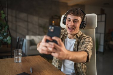 Kulaklıklı genç adam evde cep telefonuyla video görüşmesi yapıyor.