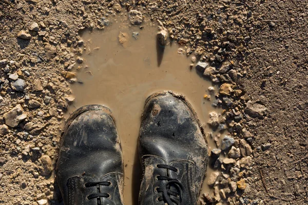 Two dirty military boots stand in a muddy puddle, suggesting a rugged environment and hard use. The boots are worn and covered in mud, adding a sense of grit and grime. The muddy water and dirty boots together create a rough and tough scene
