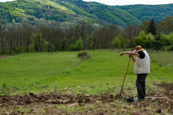 藁帽子の農家は シャベルにもたれて苦労した後に休憩を取っています 彼は田舎の春の日に畑を耕したところだ 農業の概念 — ストック写真
