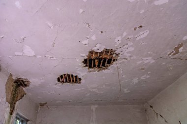 Büyük deliklerle delik deşik edilmiş eski bir binanın iç tavanı kirişleri ortaya çıkarıyor. Zaman geçişini somutlaştıran çatlaklar tavandan akıyor.