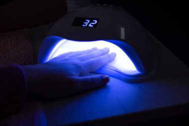 Güzellik salonunda, masanın üstünde jöle tırnaklarını iyileştiren bir kadının UV lambasının altındaki eli. Manikür kavramı