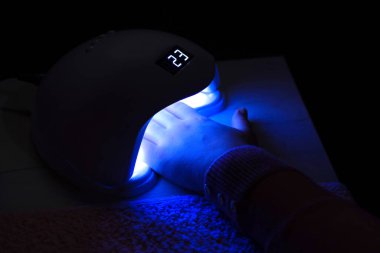 Güzellik salonundaki bir masada, daha iyi jel tırnak tedavisi için yapılan bir manikür tedavisinden sonra, UV lambasının altındaki kadın elinin yakın çekimi. Manikür kavramı