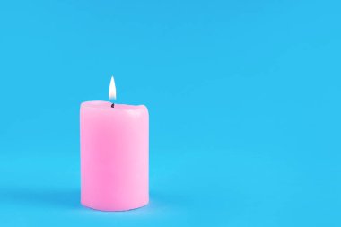 Stüdyoda klasik mavi arka planda yanan alevli pembe dekoratif mum. Metin veya tasarım için kopyalama alanı olan ateş ve minimalizm kavramı