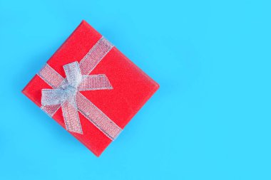 Stüdyoda klasik mavi arka planda bağlı bir kurdeleyle kırmızı hediye kutusu. Metin veya tasarım için fotokopi alanı olan Noel veya Sevgililer Günü kavramı