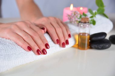 Süslemelerle çevrili bir güzellik salonundaki havluya kırmızı oje sürmüş kadın elleri. Manikür ve güzellik konsepti