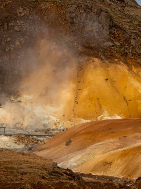İzlanda 'nın Krisuvik bölgesindeki kaynayan bir jeotermal bacadan buhar yükseliyor. Zengin toprak tonları ve engebeli dokular adaların volkanik güçlerinin iş başında olduğunu gösteriyor