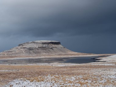 Ingjaldshlskirkja Kilisesi İzlanda 'da dramatik fırtına bulutlarının altında karlı bir tepede. Snfellsnes Yarımadası 'ndaki kırmızı çatılı şapel ve karanlık kış gökyüzü arasında çarpıcı bir tezat