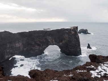Ingjaldshlskirkja Kilisesi İzlanda 'da dramatik fırtına bulutlarının altında karlı bir tepede. Snfellsnes Yarımadası 'ndaki kırmızı çatılı şapel ve karanlık kış gökyüzü arasında çarpıcı bir tezat