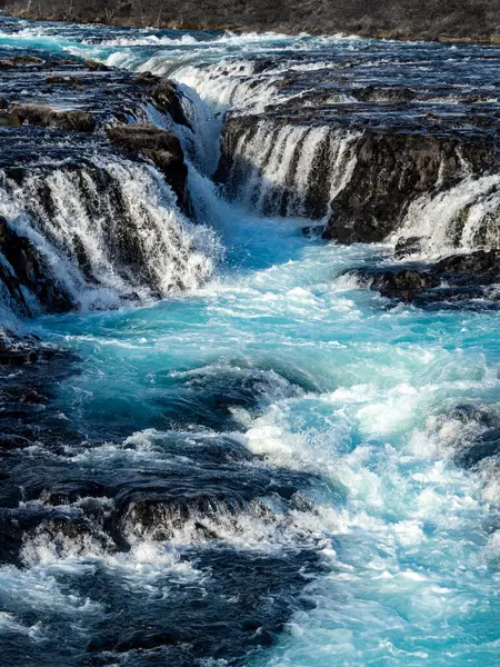 İzlanda 'da Bruarafoss Şelalesi' nin yakın çekimleri, engebeli kayaların üzerinden akan canlı turkuaz suyu sergiliyor. Kış manzarasının doğal bir başyapıtı.