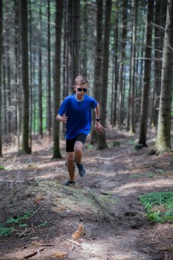 Genç bir adam ormanda bir yol boyunca koşar..