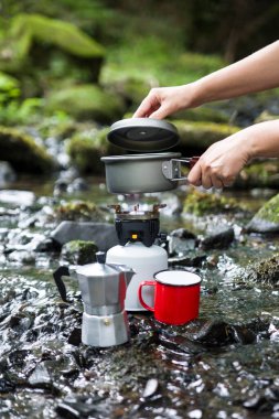 Kahve demliği ve metal bardak dağ nehrinin arka planına karşı büyük taşın üzerinde. Kahve demliği taştan tabakta, bulanık arka plan..