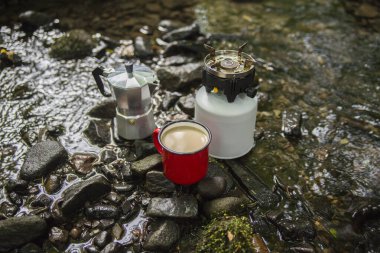 Kahve demliği ve metal bardak dağ nehrinin arka planına karşı büyük taşın üzerinde. Kahve demliği taştan tabakta, bulanık arka plan..