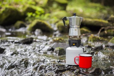 Kahve demliği ve metal bardak dağ nehrinin arka planına karşı büyük taşın üzerinde. Kahve demliği taştan tabakta, bulanık arka plan..