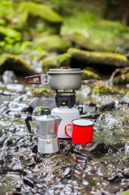 Kahve demliği ve metal bardak dağ nehrinin arka planına karşı büyük taşın üzerinde. Kahve demliği taştan tabakta, bulanık arka plan..