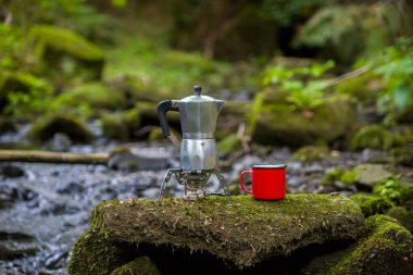 Kahve demliği ve metal bardak dağ nehrinin arka planına karşı büyük taşın üzerinde. Kahve demliği taştan tabakta, bulanık arka plan..