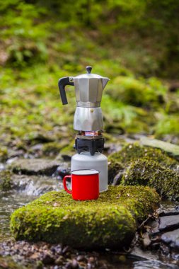 Kahve demliği ve metal bardak dağ nehrinin arka planına karşı büyük taşın üzerinde. Kahve demliği taştan tabakta, bulanık arka plan..