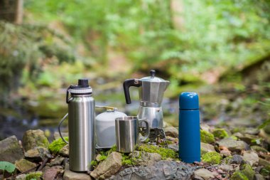 Kahve demliği ve metal bardak dağ nehrinin arka planına karşı büyük taşın üzerinde. Kahve demliği taştan tabakta, bulanık arka plan..