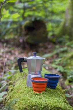 Bir dağ nehrinin arka planında büyük bir taşın üzerinde kahve fincanı ve metal bardak. Doğanın bulanık arka planına karşı taş bir levhanın üzerinde kahve demliği..