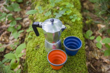 Bir dağ nehrinin arka planında büyük bir taşın üzerinde kahve fincanı ve metal bardak. Doğanın bulanık arka planına karşı taş bir levhanın üzerinde kahve demliği..