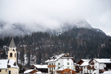 Heavy snow clouds hang over the snow-covered mountains and fir trees in the small mountain tourist village