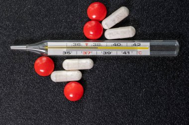 Bir termometre, yüksek sıcaklık ve siyah bir masada kırmızı ve beyaz tabletler.