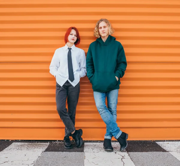 两个高加索青少年朋友站在橙色墙的背景旁边拍照时的肖像 粗心大意的年轻人 时间概念图像 — 图库照片