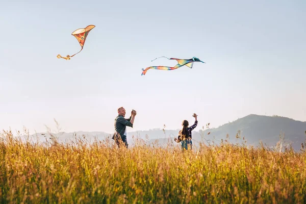 在高高的草地上放飞五彩缤纷的风筝时 带着女儿微笑着父亲 温暖的家庭夏季户外拍照或户外消磨时间的概念形象 — 图库照片