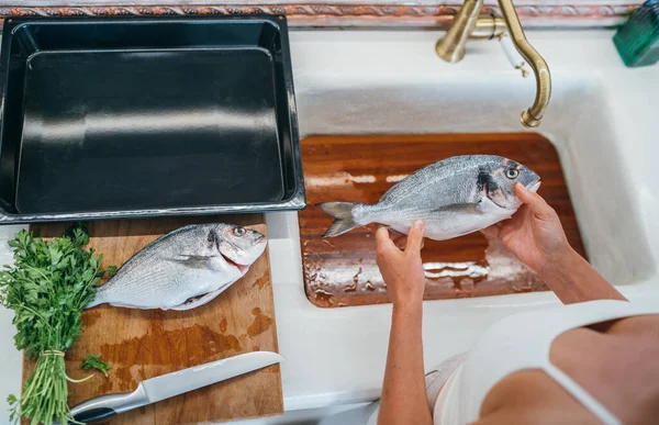 台所の洗面台の水の下の切口の後の新鮮なOrataかDorada魚のクリーニング 調理用に用意されたベーキングシート 健康的な新鮮な魚介類の準備画像 — ストック写真