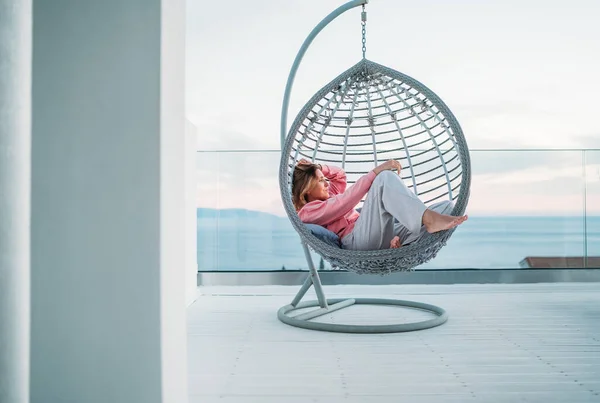 美丽的中年妇女赤脚躺在露天平台上舒适的悬挂椅上 享受夕阳西下的阳光 现代家庭生活方式和心理健康概念形象 — 图库照片